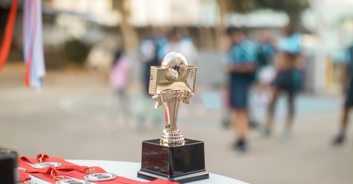 Close-up of a polished soccer trophy with medals at an outdoor sports award ceremony.
